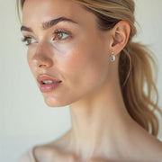 Close-up of a woman's face with a neutral background wearing yellow gold  earrings with blue sapphire and white diamonds in a drop cluster