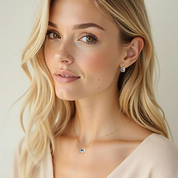 Woman with blonde hair wearing a necklace and earrings against a neutral background