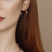 Close-up of a person wearing gold hoop earrings with a neutral background