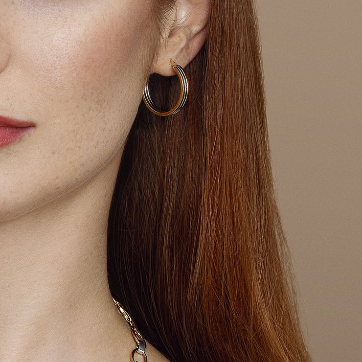 Close-up of a person wearing gold hoop earrings with a neutral background