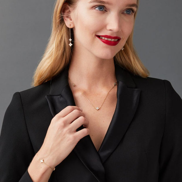 Woman wearing a black blazer with yellow gold mother of pearl clover jewellery on a gray background