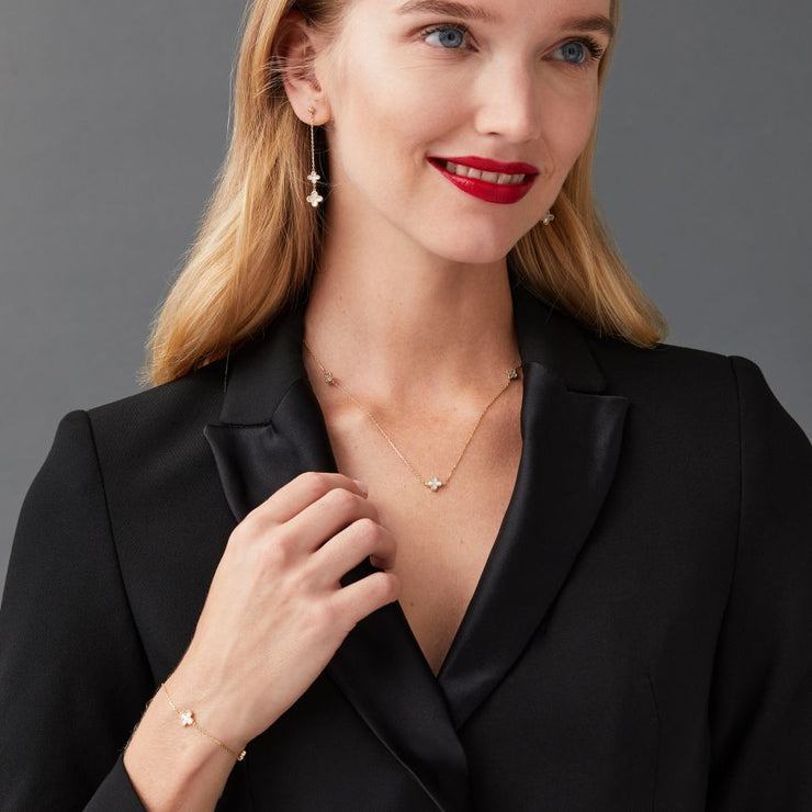 Woman wearing a black blazer with yellow gold mother of pearl clover jewellery on a gray background